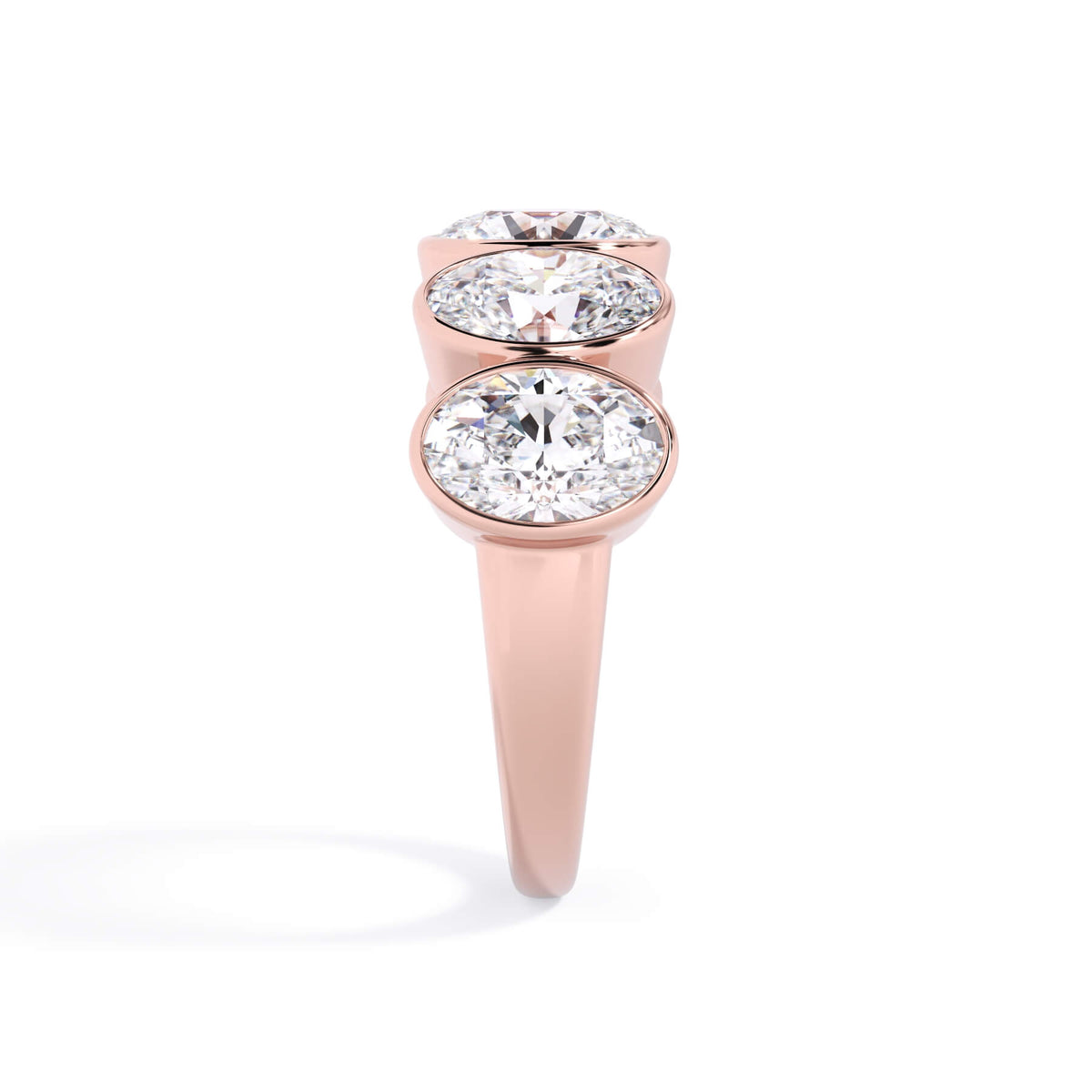 A picture of a five stone diamond wedding ring with oval shape diamonds that are bezel set in rose gold on a white background with a side profile view.