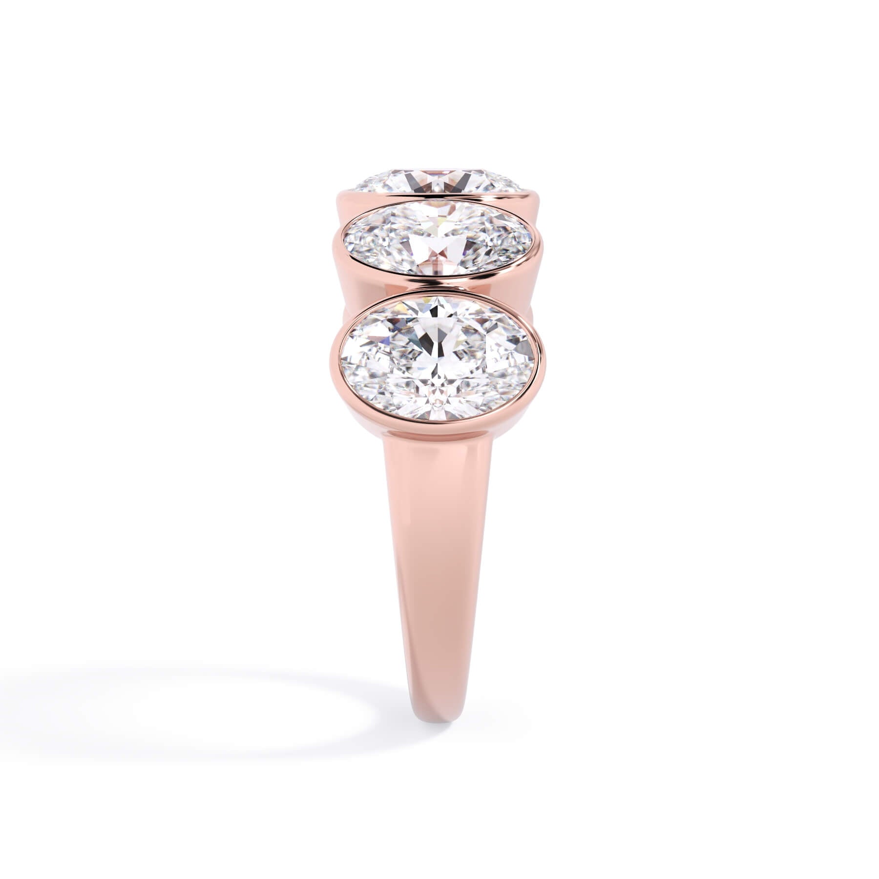 A picture of a five stone diamond wedding ring with oval shape diamonds that are bezel set in rose gold on a white background with a side profile view.