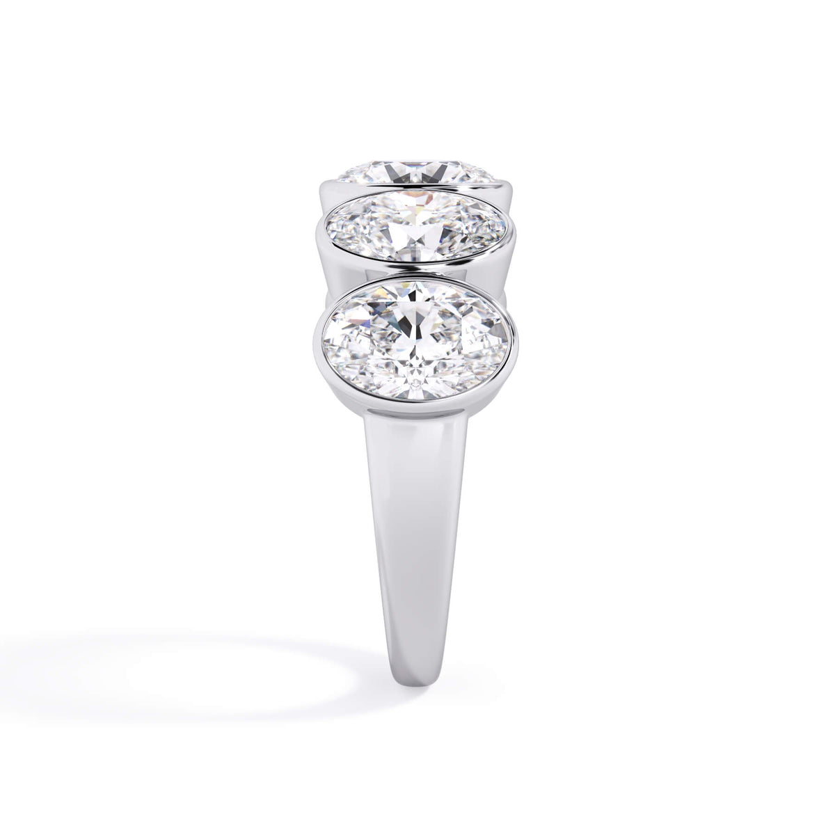 A picture of a five stone diamond wedding ring with oval shape diamonds that are bezel set in white gold or platinum on a white background with a side profile view.