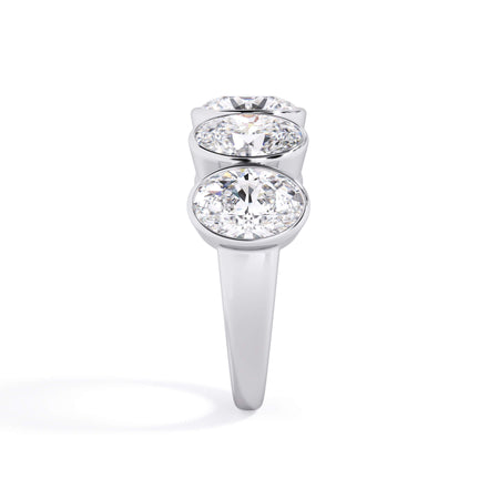 A picture of a five stone diamond wedding ring with oval shape diamonds that are bezel set in white gold or platinum on a white background with a side profile view.