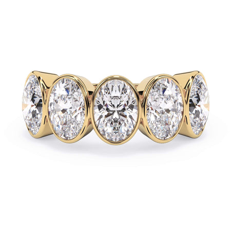 A picture of a five stone diamond wedding ring with oval shape diamonds that are bezel set in yellow gold on a white background with the ring facing forward, lying down.