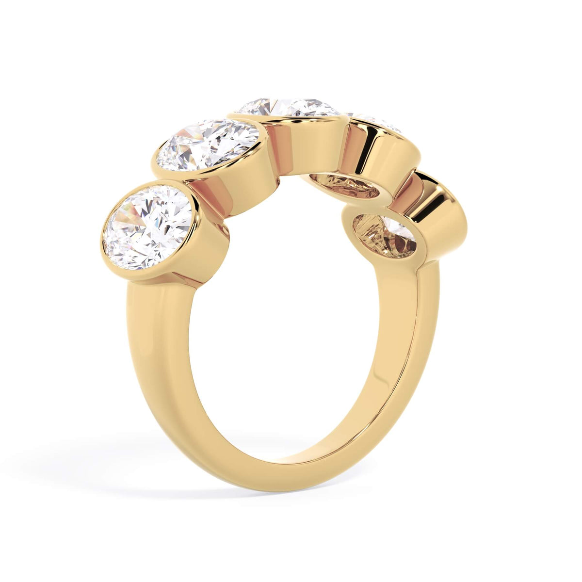 A picture of a five stone diamond wedding ring with oval shape diamonds that are bezel set in yellow gold on a white background with a slightly angled, through the finger view.