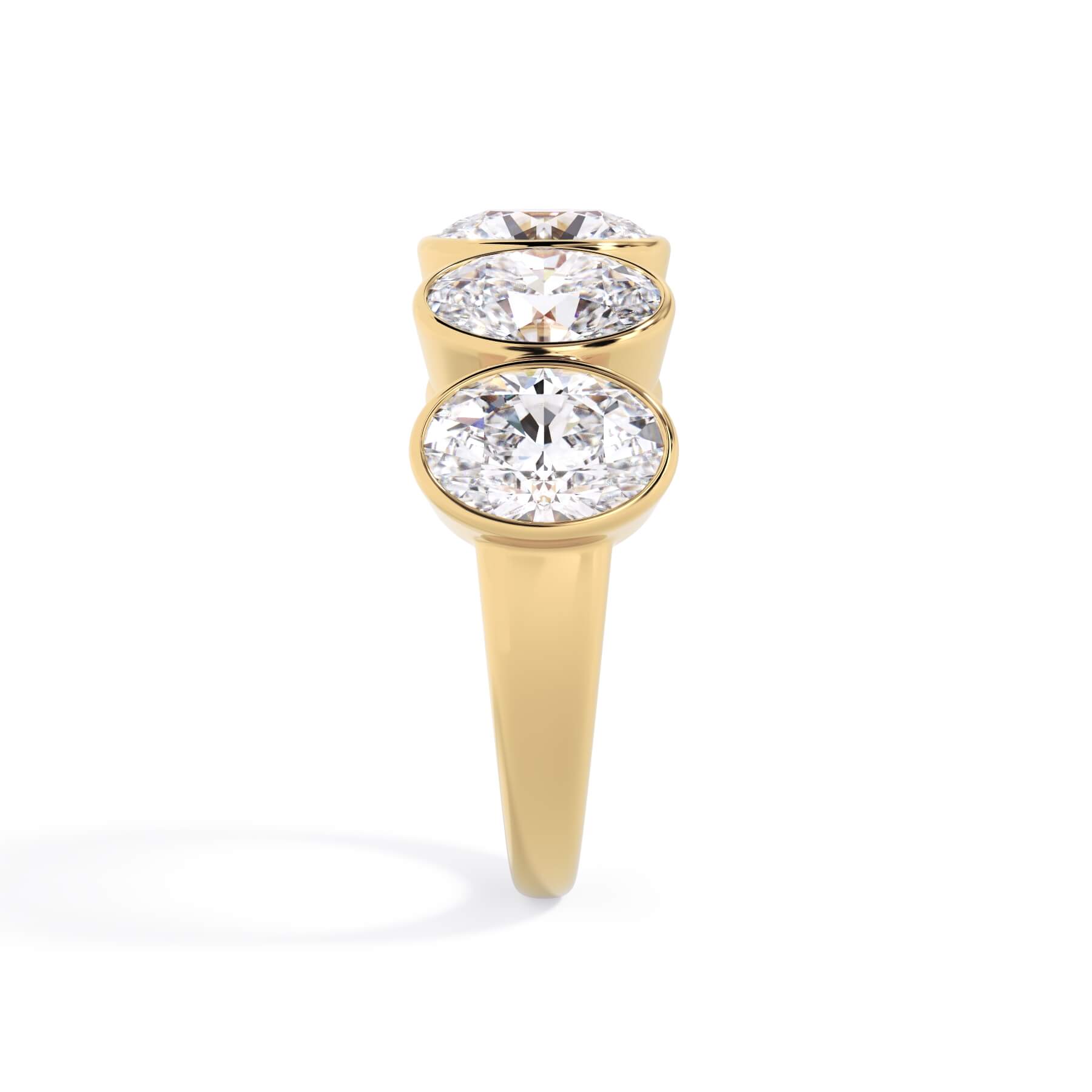A picture of a five stone diamond wedding ring with oval shape diamonds that are bezel set in yellow gold on a white background with a side profile view.