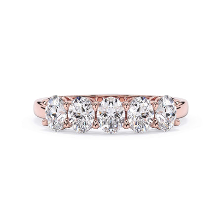 A picture of a five stone diamond wedding ring with oval shape diamonds that are shared prong set in rose gold on a white background with the ring facing forward, lying down.