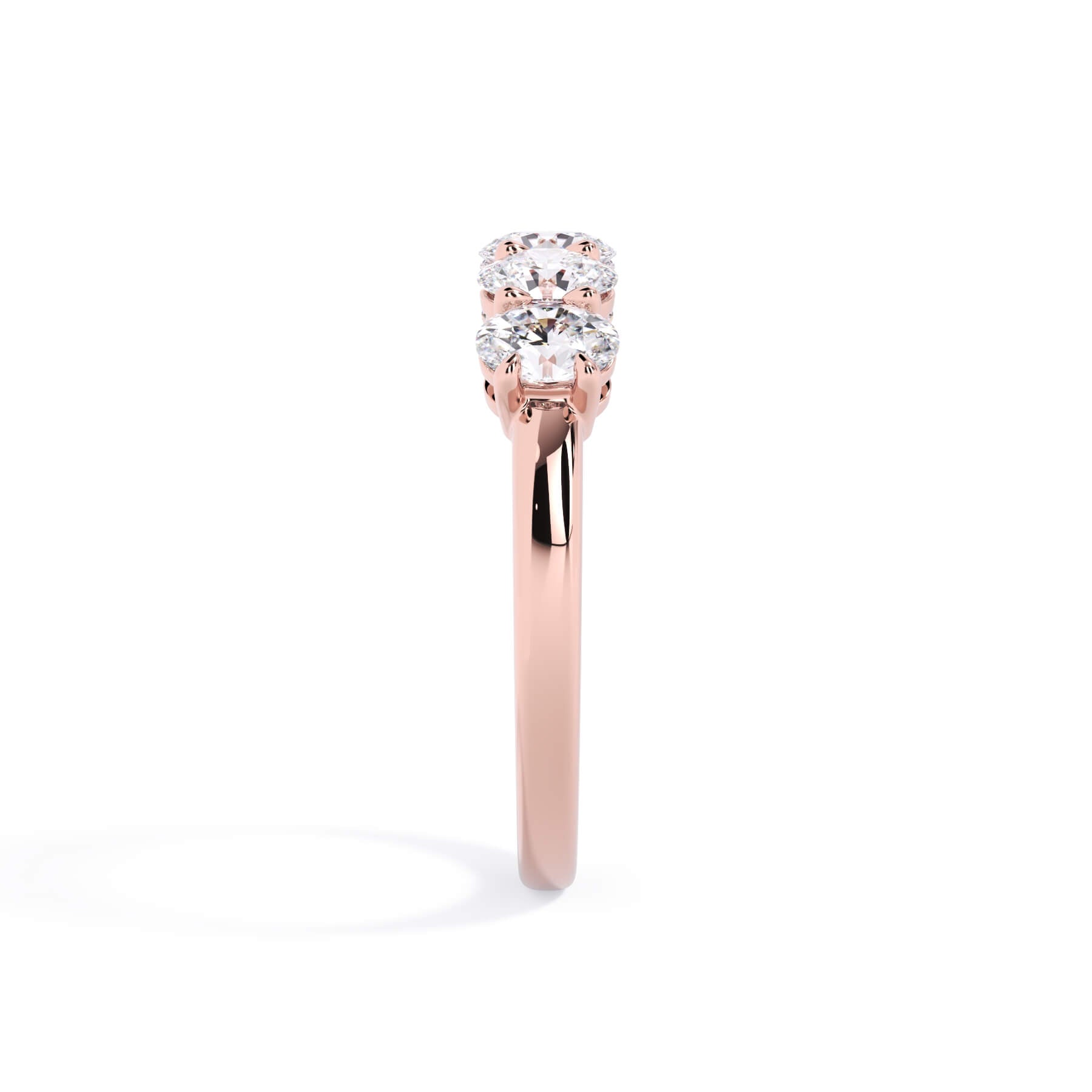 A picture of a five stone diamond wedding ring with oval shape diamonds that are shared prong set in rose gold on a white background with a side profile view.