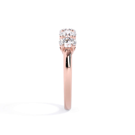A picture of a five stone diamond wedding ring with oval shape diamonds that are shared prong set in rose gold on a white background with a side profile view.