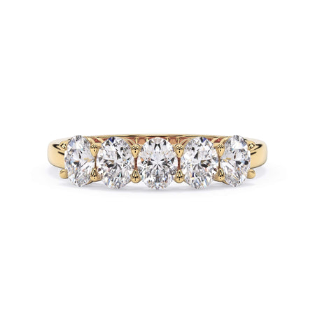 A picture of a five stone diamond wedding ring with oval shape diamonds that are shared prong set in yellow gold on a white background with the ring facing forward, lying down.