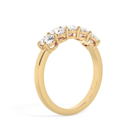 A picture of a five stone diamond wedding ring with oval shape diamonds that are shared prong set in yellow gold on a white background with a slightly angled, through the finger view.