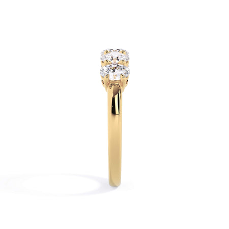 A picture of a five stone diamond wedding ring with oval shape diamonds that are shared prong set in yellow gold on a white background with a side profile view.