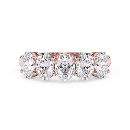 A picture of a five stone diamond wedding ring with oval shape diamonds that are shared prong set in rose gold on a white background with the ring facing forward, lying down.