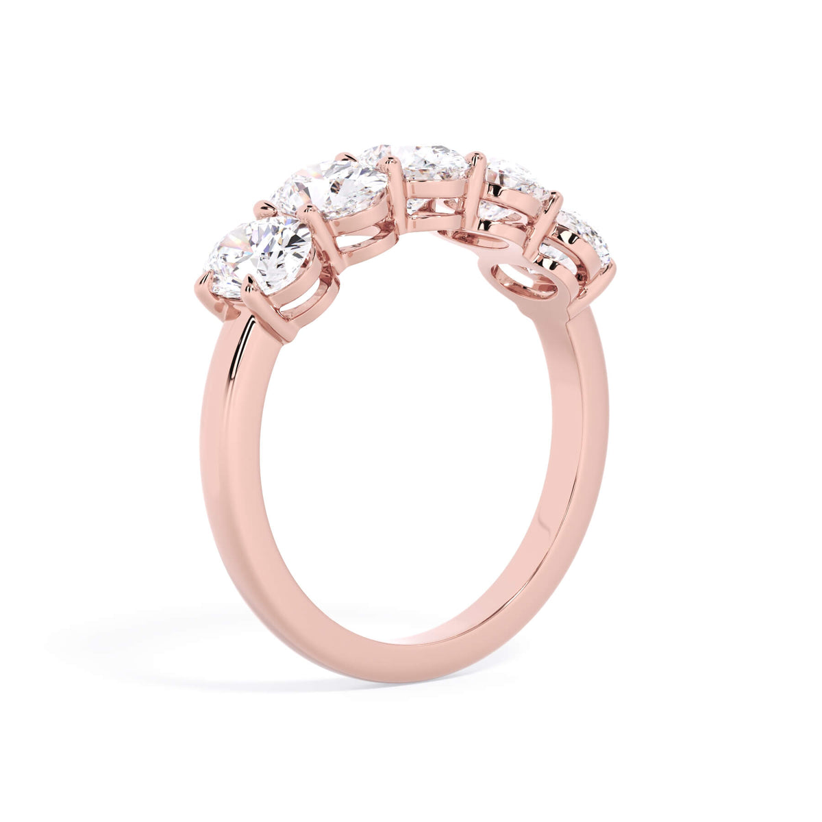 A picture of a five stone diamond wedding ring with oval shape diamonds that are shared prong set in rose gold on a white background with a slightly angled, through the finger view.