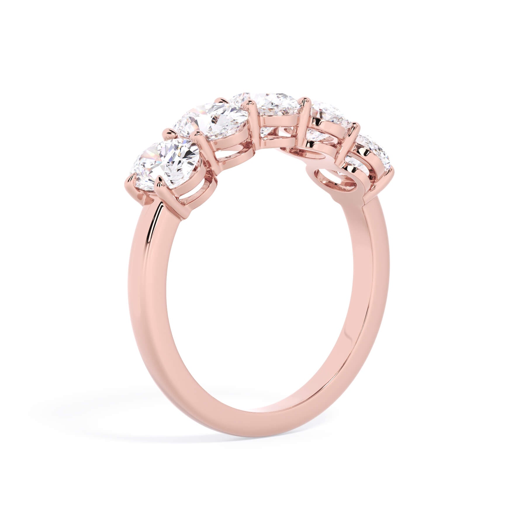 A picture of a five stone diamond wedding ring with oval shape diamonds that are shared prong set in rose gold on a white background with a slightly angled, through the finger view.