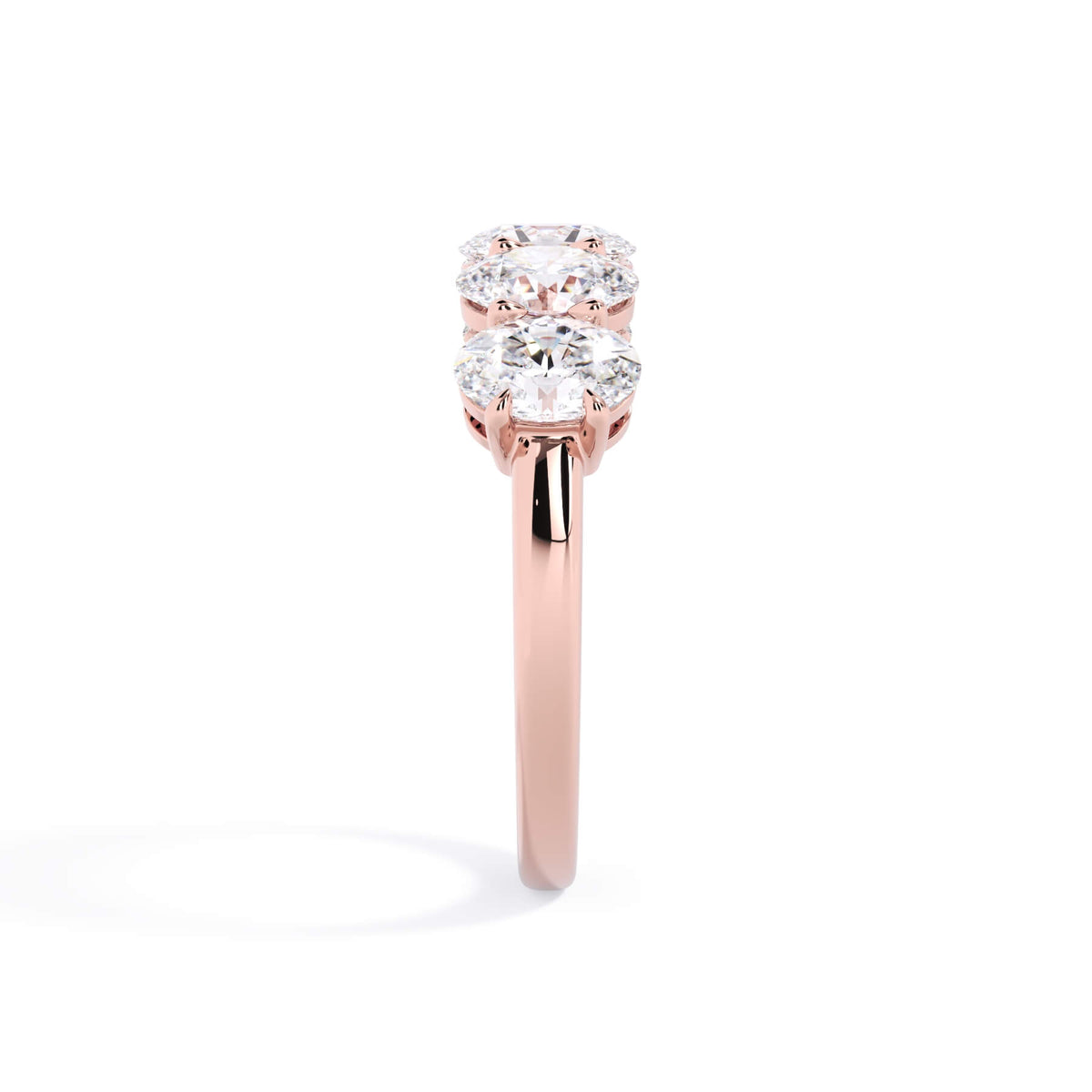 A picture of a five stone diamond wedding ring with oval shape diamonds that are shared prong set in rose gold on a white background with a side profile view.