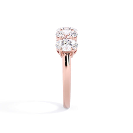 A picture of a five stone diamond wedding ring with oval shape diamonds that are shared prong set in rose gold on a white background with a side profile view.