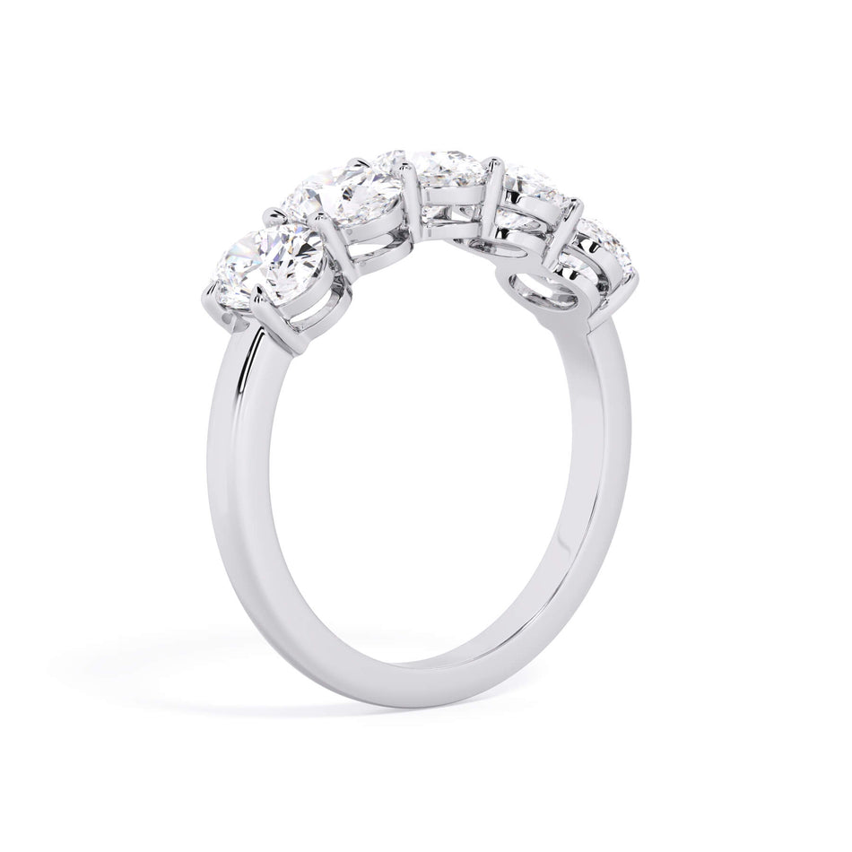 A picture of a five stone diamond wedding ring with oval shape diamonds that are shared prong set in white gold or platinum on a white background with a slightly angled, through the finger view.