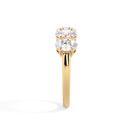 A picture of a five stone diamond wedding ring with oval shape diamonds that are shared prong set in yellow gold on a white background with a side profile view.