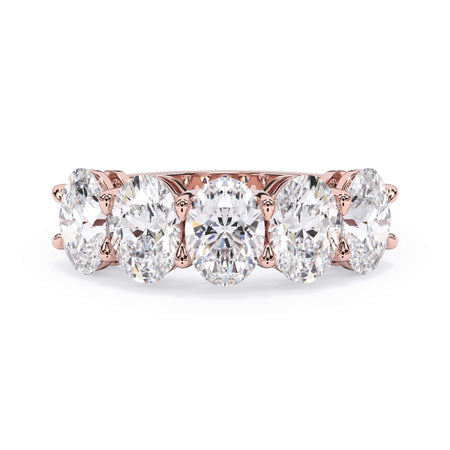 A picture of a five stone diamond wedding ring with oval shape diamonds that are shared prong set in rose gold on a white background with the ring facing forward, lying down.