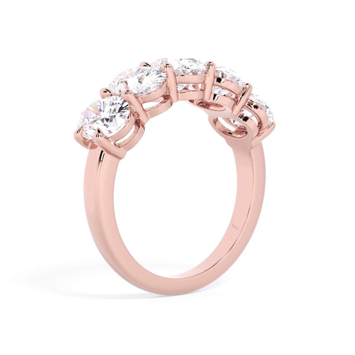 A picture of a five stone diamond wedding ring with oval shape diamonds that are shared prong set in rose gold on a white background with a slightly angled, through the finger view.