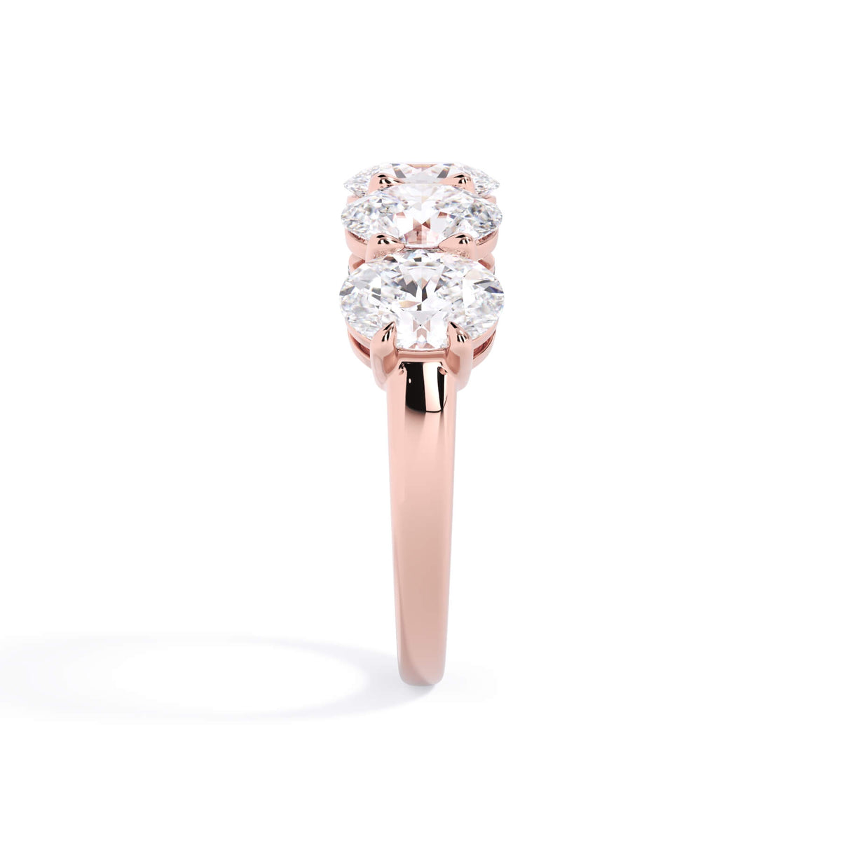 A picture of a five stone diamond wedding ring with oval shape diamonds that are shared prong set in rose gold on a white background with a side profile view.