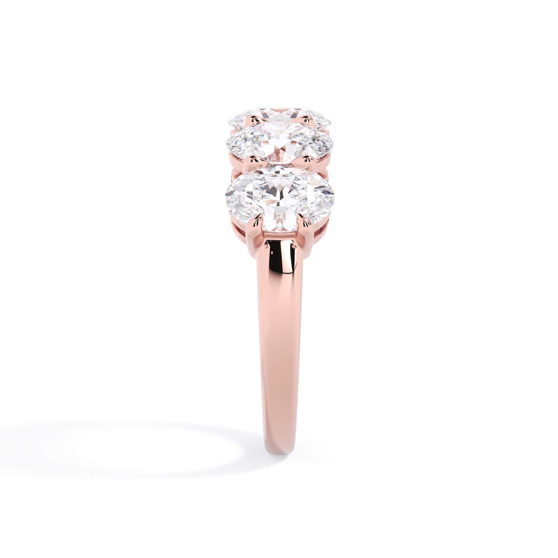 A picture of a five stone diamond wedding ring with oval shape diamonds that are shared prong set in rose gold on a white background with a side profile view.