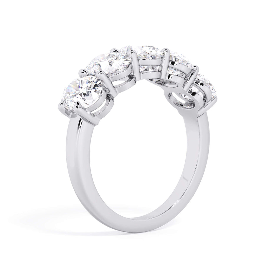 A picture of a five stone diamond wedding ring with oval shape diamonds that are shared prong set in white gold or platinum on a white background with a slightly angled, through the finger view.