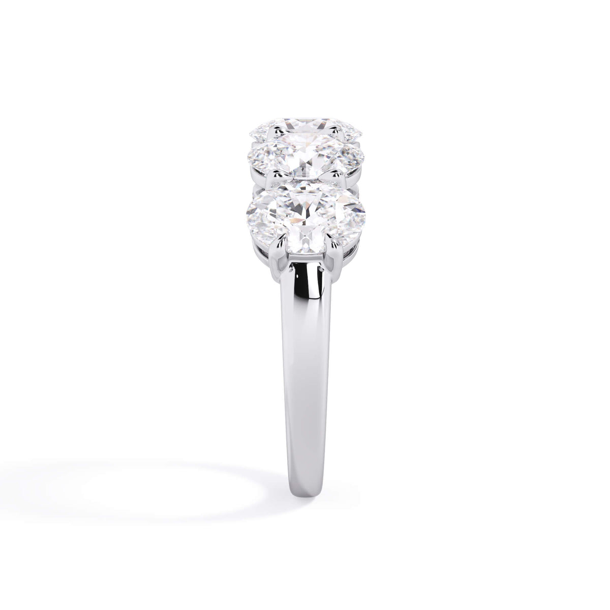 A picture of a five stone diamond wedding ring with oval shape diamonds that are shared prong set in white gold or platinum on a white background with a side profile view.