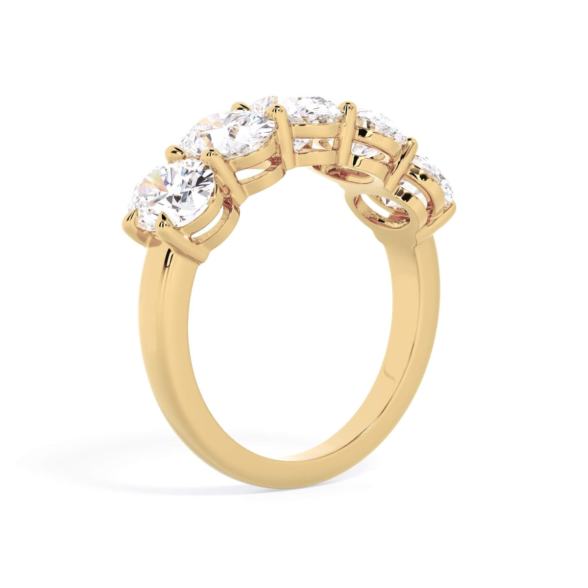 A picture of a five stone diamond wedding ring with oval shape diamonds that are shared prong set in yellow gold on a white background with a slightly angled, through the finger view.