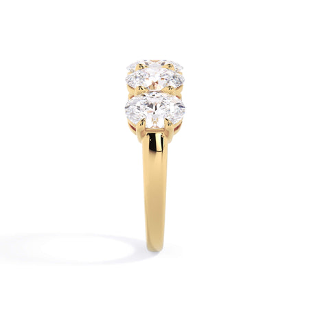 A picture of a five stone diamond wedding ring with oval shape diamonds that are shared prong set in yellow gold on a white background with a side profile view.