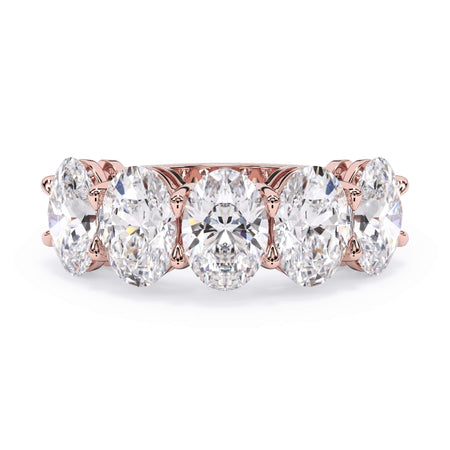A picture of a five stone diamond wedding ring with oval shape diamonds that are shared prong set in rose gold on a white background with the ring facing forward, lying down.