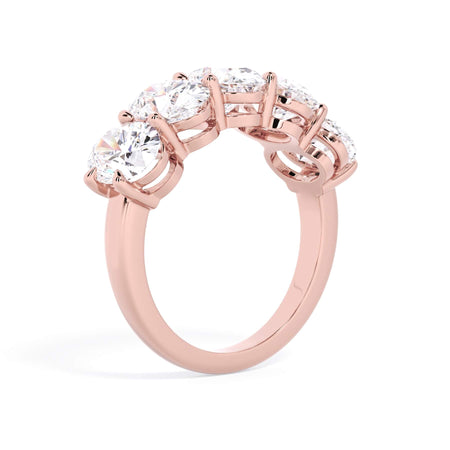A picture of a five stone diamond wedding ring with oval shape diamonds that are shared prong set in rose gold on a white background with a slightly angled, through the finger view.