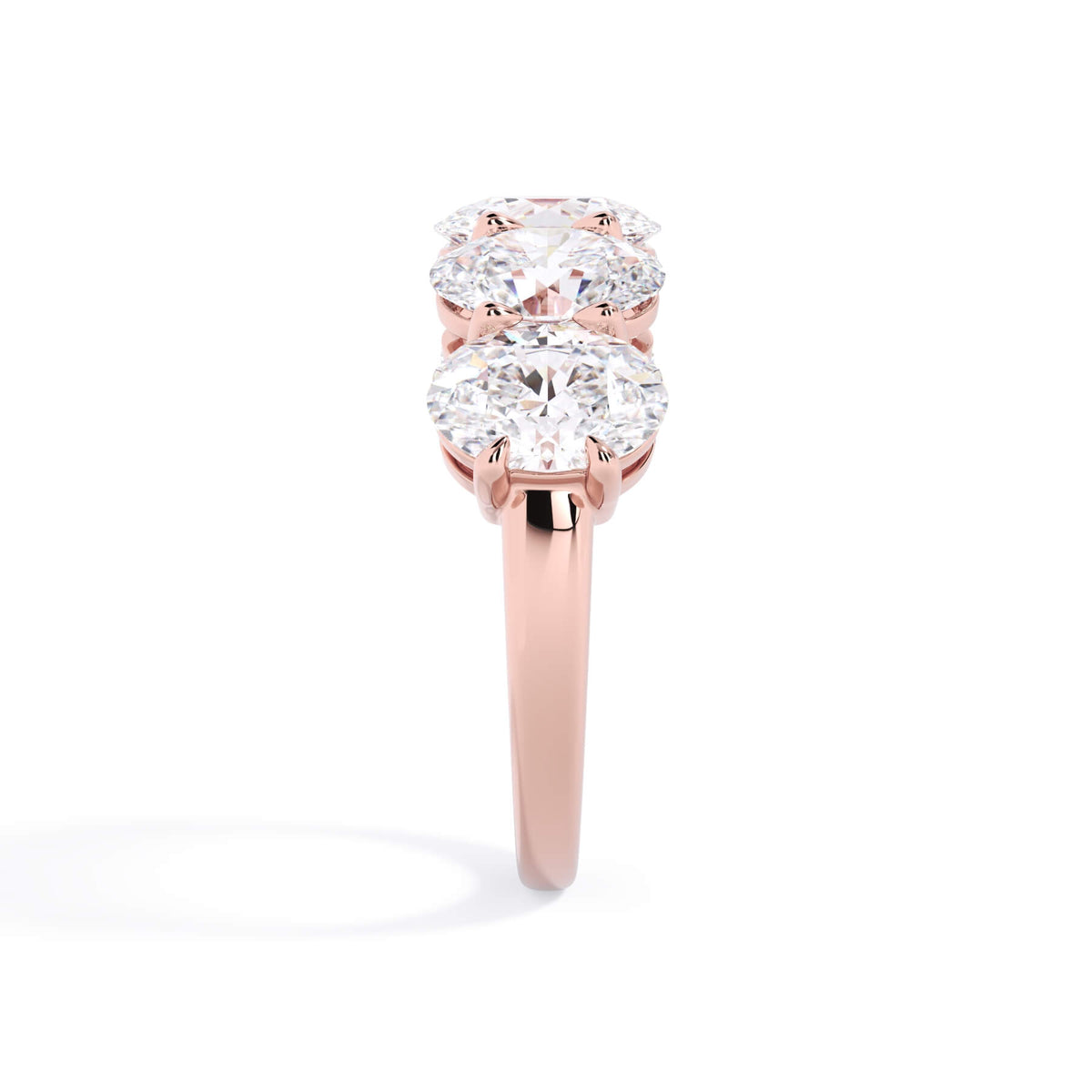 A picture of a five stone diamond wedding ring with oval shape diamonds that are shared prong set in rose gold on a white background with a side profile view.