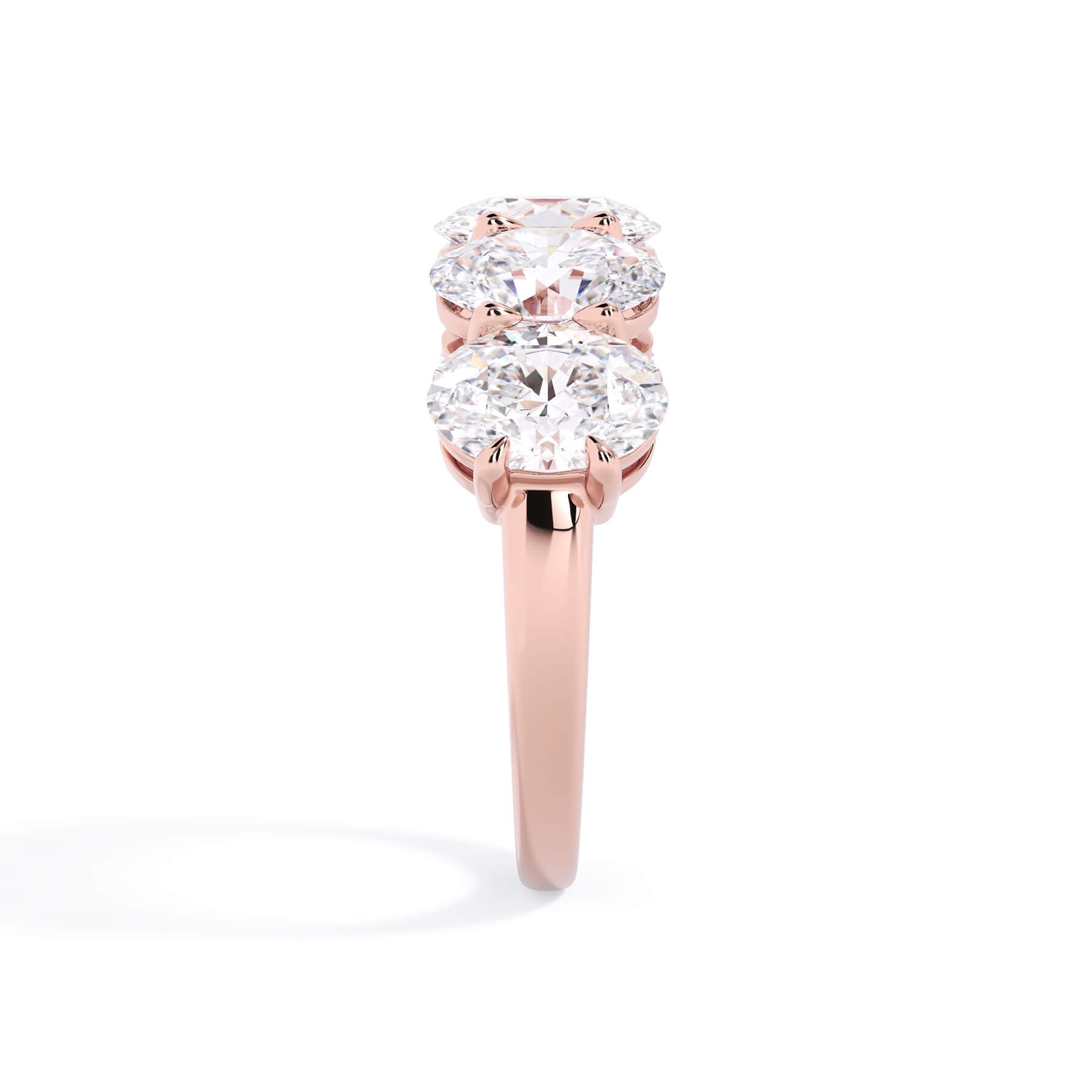A picture of a five stone diamond wedding ring with oval shape diamonds that are shared prong set in rose gold on a white background with a side profile view.