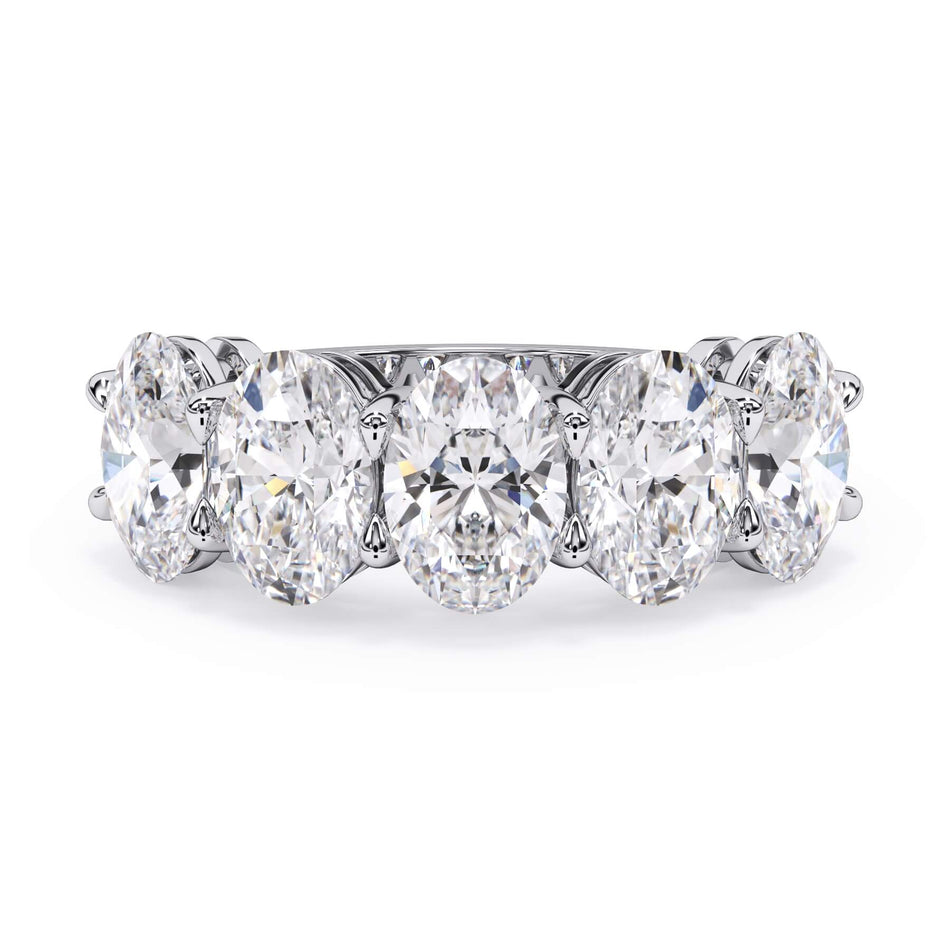 A picture of a five stone diamond wedding ring with oval shape diamonds that are shared prong set in white gold or platinum on a white background with the ring facing forward, lying down.