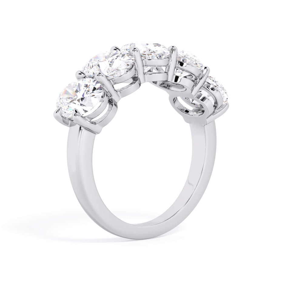 A picture of a five stone diamond wedding ring with oval shape diamonds that are shared prong set in white gold or platinum on a white background with a slightly angled, through the finger view.