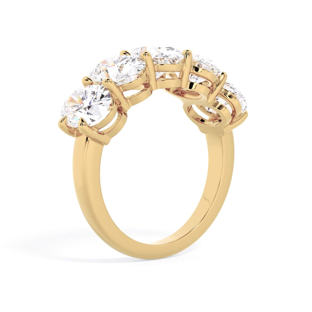 A picture of a five stone diamond wedding ring with oval shape diamonds that are shared prong set in yellow gold on a white background with a slightly angled, through the finger view.