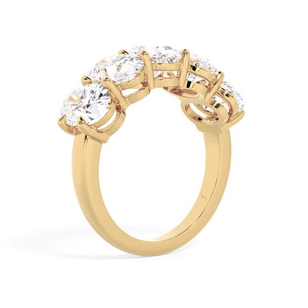 A picture of a five stone diamond wedding ring with oval shape diamonds that are shared prong set in yellow gold on a white background with a slightly angled, through the finger view.