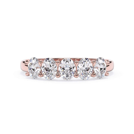 A picture of a five stone diamond wedding ring with oval shape diamonds that are u prong set in rose gold on a white background with the ring facing forward, lying down.