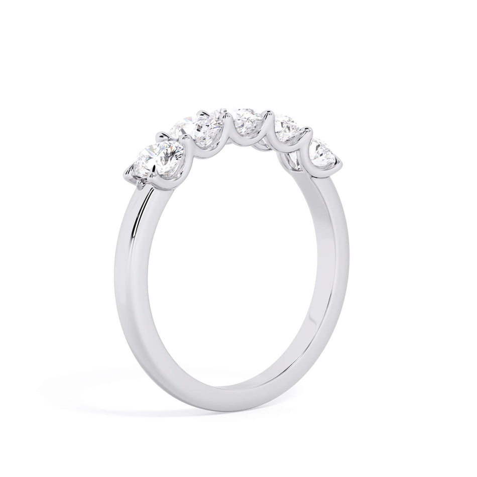 A picture of a five stone diamond wedding ring with oval shape diamonds that are u prong set in white gold or platinum on a white background with a slightly angled, through the finger view.