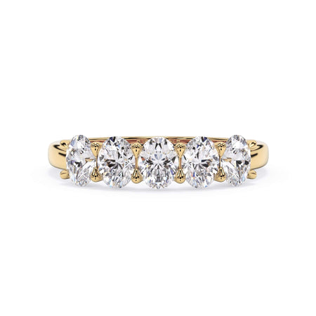 A picture of a five stone diamond wedding ring with oval shape diamonds that are u prong set in yellow gold on a white background with the ring facing forward, lying down.