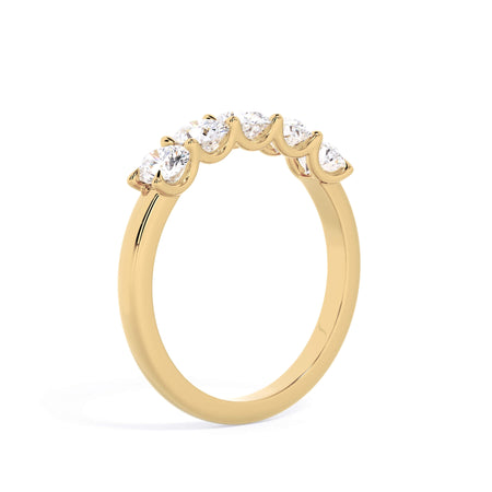 A picture of a five stone diamond wedding ring with oval shape diamonds that are u prong set in yellow gold on a white background with a slightly angled, through the finger view.