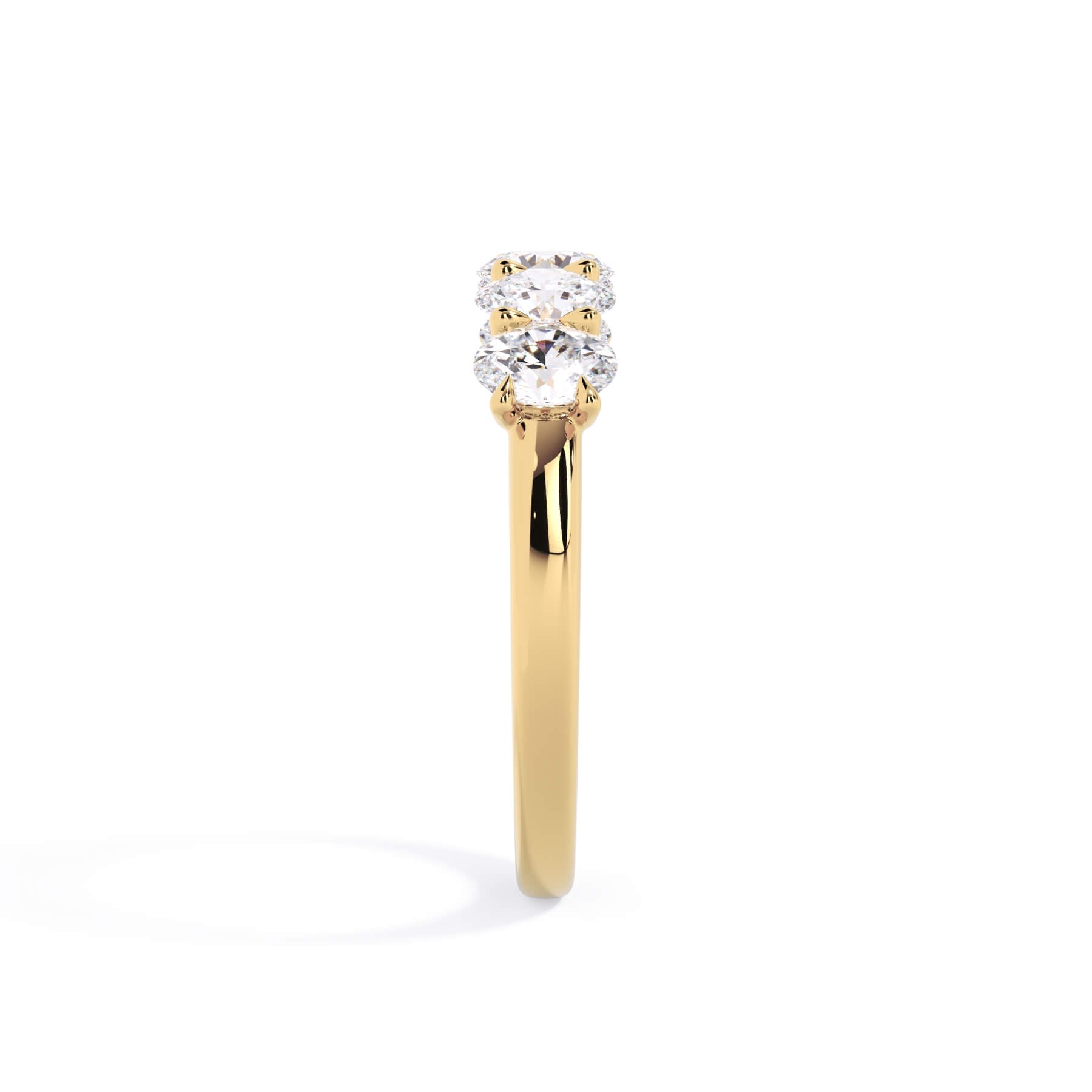 A picture of a five stone diamond wedding ring with oval shape diamonds that are u prong set in yellow gold on a white background with a side profile view.