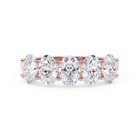 A picture of a five stone diamond wedding ring with oval shape diamonds that are u prong set in rose gold on a white background with the ring facing forward, lying down.