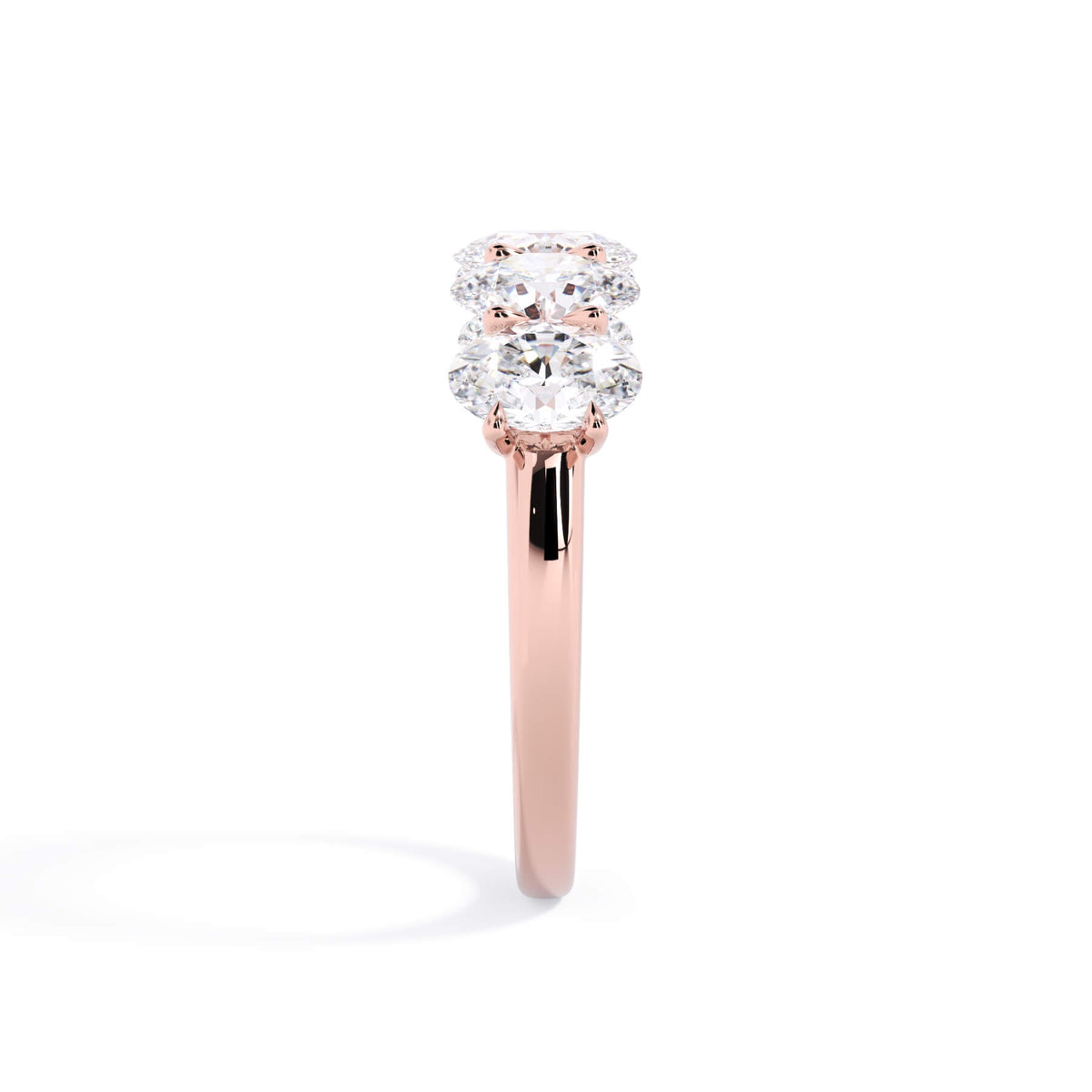 A picture of a five stone diamond wedding ring with oval shape diamonds that are u prong set in rose gold on a white background with a side profile view.