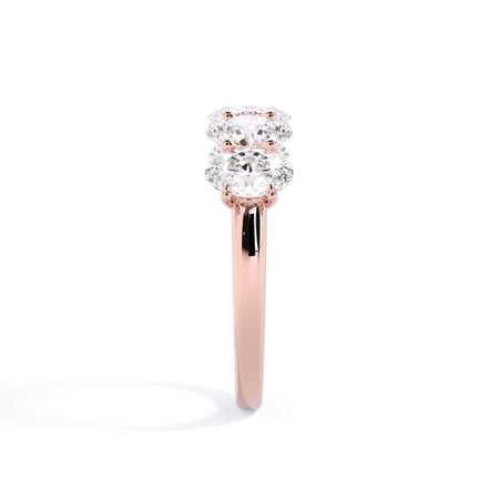 A picture of a five stone diamond wedding ring with oval shape diamonds that are u prong set in rose gold on a white background with a side profile view.