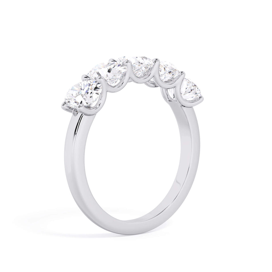 A picture of a five stone diamond wedding ring with oval shape diamonds that are u prong set in white gold or platinum on a white background with a slightly angled, through the finger view.