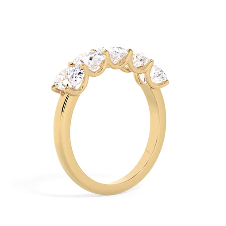 A picture of a five stone diamond wedding ring with oval shape diamonds that are u prong set in yellow gold on a white background with a slightly angled, through the finger view.