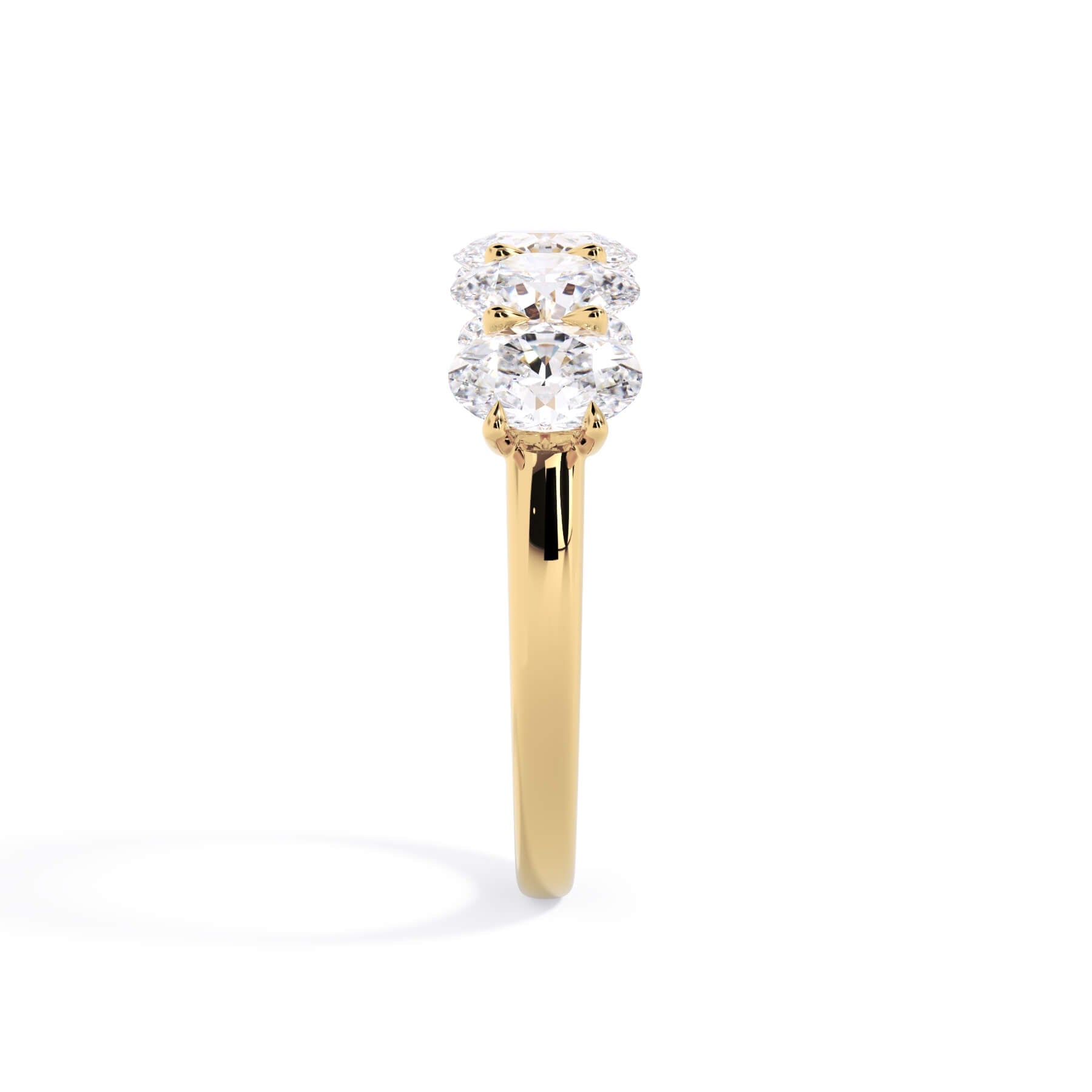 A picture of a five stone diamond wedding ring with oval shape diamonds that are u prong set in yellow gold on a white background with a side profile view.