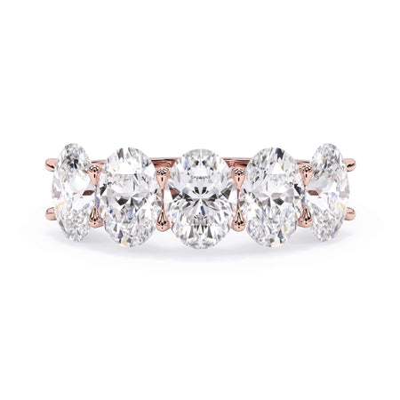 A picture of a five stone diamond wedding ring with oval shape diamonds that are u prong set in rose gold on a white background with the ring facing forward, lying down.