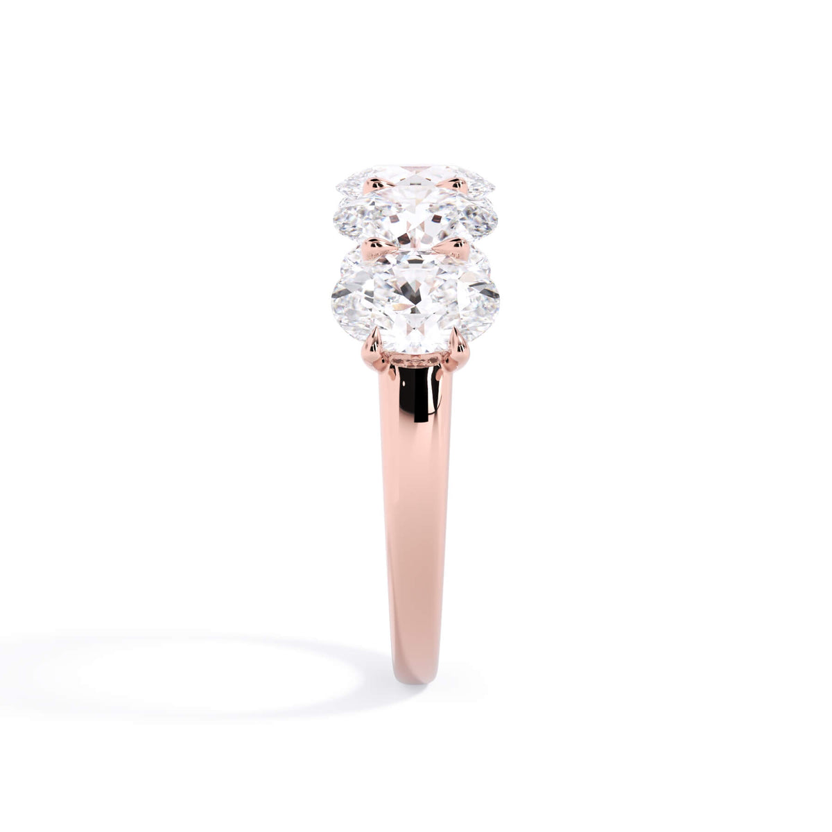 A picture of a five stone diamond wedding ring with oval shape diamonds that are u prong set in rose gold on a white background with a side profile view.