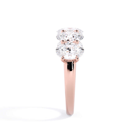A picture of a five stone diamond wedding ring with oval shape diamonds that are u prong set in rose gold on a white background with a side profile view.